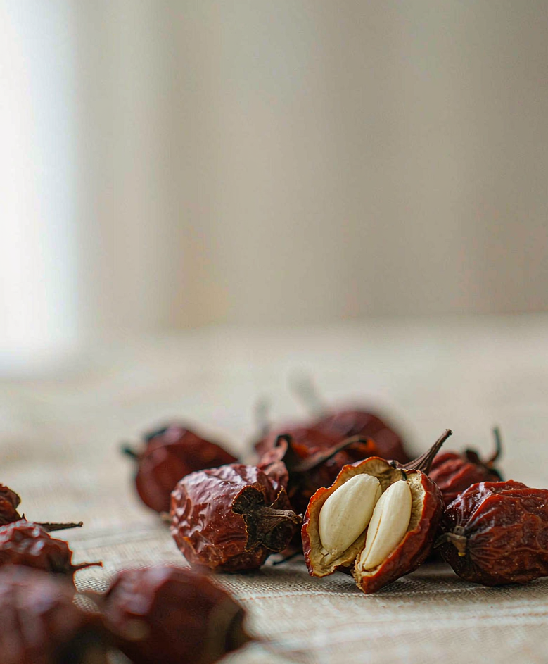 Photograph of dried wild jujube fruits with one split open revealing paired pale seed kernels — suanzaoren as it appears in real life
