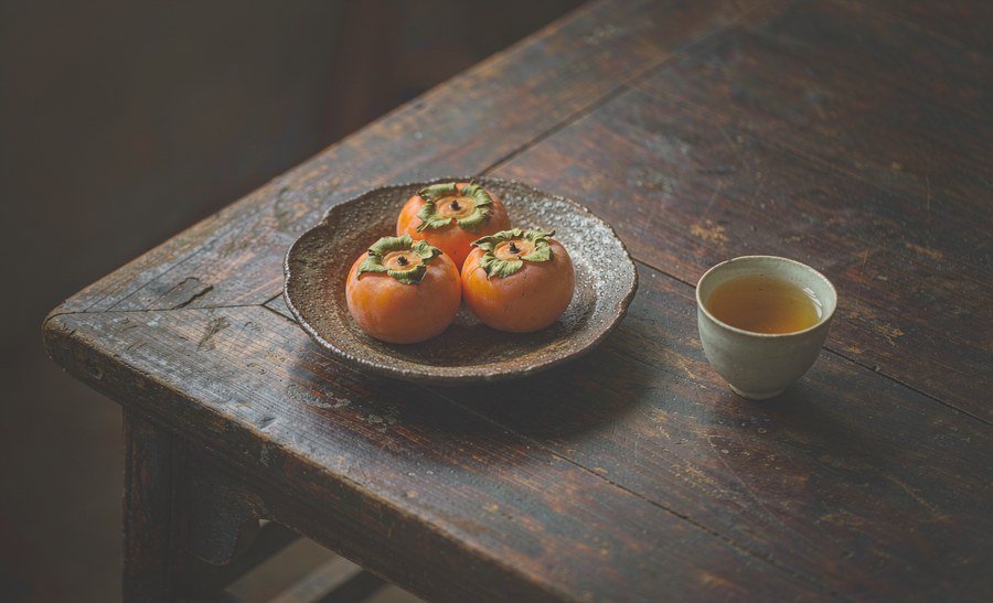 persimmons on a plate beside a cup of herbal tea in late afternoon light, Chinese ink-wash style